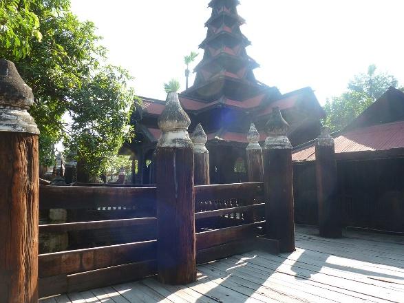 A wooden fence with ornate posts stands before a tiered, pagoda-like building with a red roof.