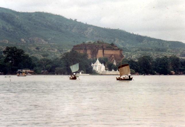 A wide shot shows a hazy river with two sailboats, a temple, and a lush green mountainside in the background.