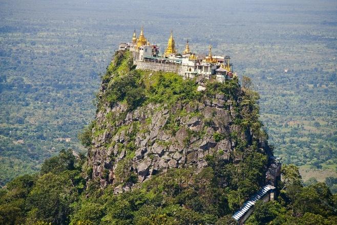 A Buddhist monastery perches atop a steep, verdant mountain, accessible by a long staircase.