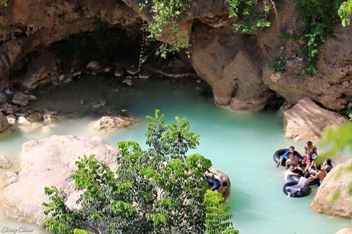 A group of people enjoy a refreshing swim in a clear turquoise pool nestled within a rocky canyon.