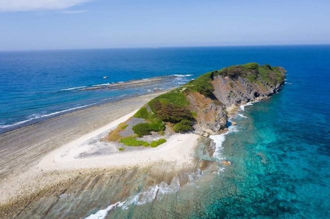 An aerial view captures a lush green island with rugged cliffs meeting the turquoise ocean.