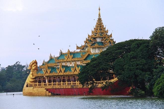 A golden dragon-headed boat-shaped building with green tiered roofs sits on the water, with lush trees surrounding it.