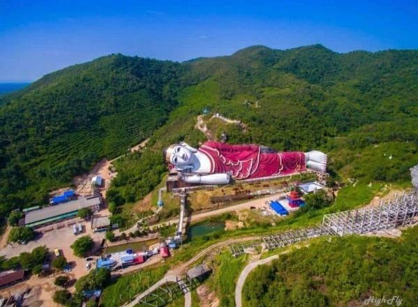 An aerial view of the magnificent reclining Buddha statue situated on a lush green hillside under a clear blue sky.
