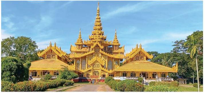 A magnificent golden Buddhist temple complex with intricate tiered roofs and spires stands majestically under a clear blue sky.