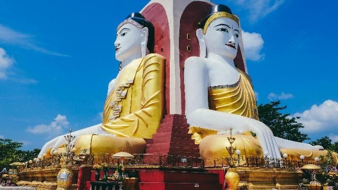 Two giant, gilded Buddha statues stand against a bright blue sky with scattered clouds.