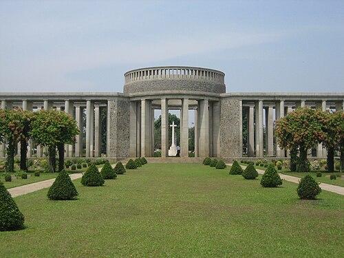 A grand stone memorial with a circular facade and colonnade stands behind a neatly manicured lawn with symmetrical trees.